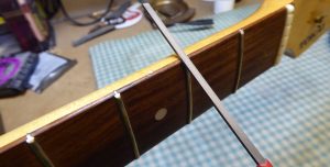 Very carefully using a fine file to smooth the sharp fret ends on a Tokai "Stratocaster.